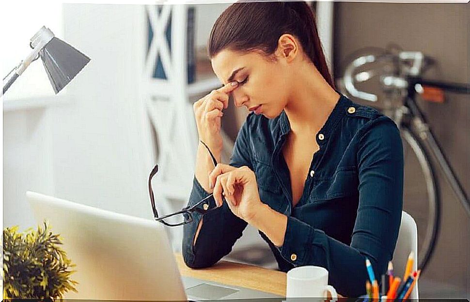 Woman in front of pc with hand on temples