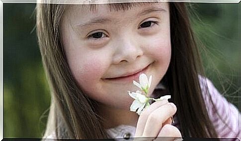 Down girl holds flower in hand in front of mouth.