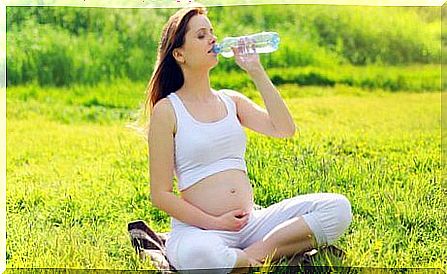 Pregnant woman drinking water sitting on the lawn.